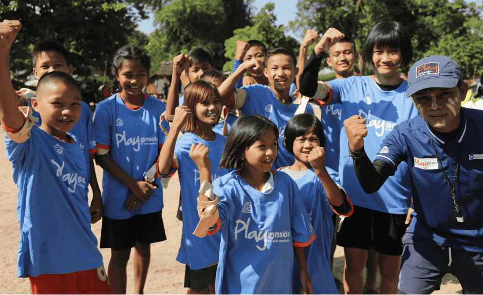 Ein junges Fußball Team steht lächelnd zusammen in einer Gruppe. Einige halten stolz ihre Fäuste nach oben.