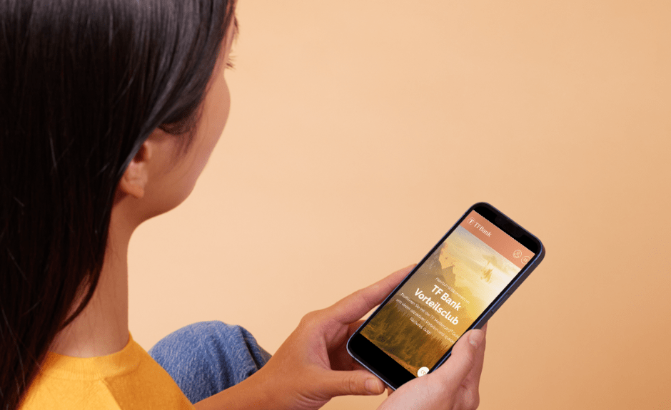 Frau schaut auf ihr Handy und die TF Bank Mobile App.