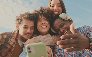 Freunde schauen lachend zusammen in ein Smartphone und umarmen sich.