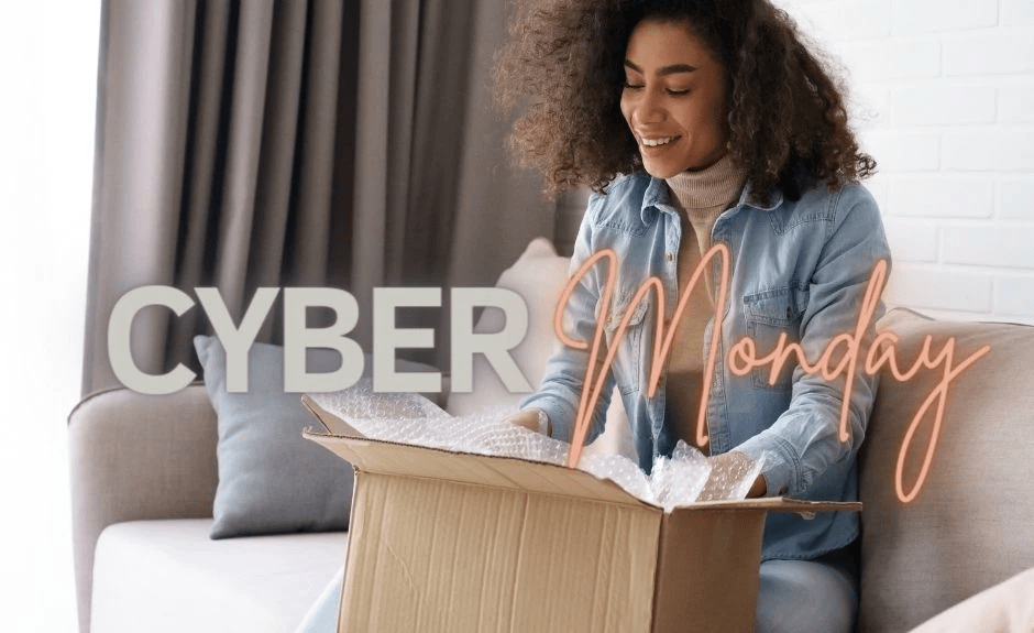 Frau sitzt auf Couch und schaut lächelnd in einen geöffneten Karton und packt etwas aus. Auf dem Bild ist der Schriftzug "Cyber Monday".