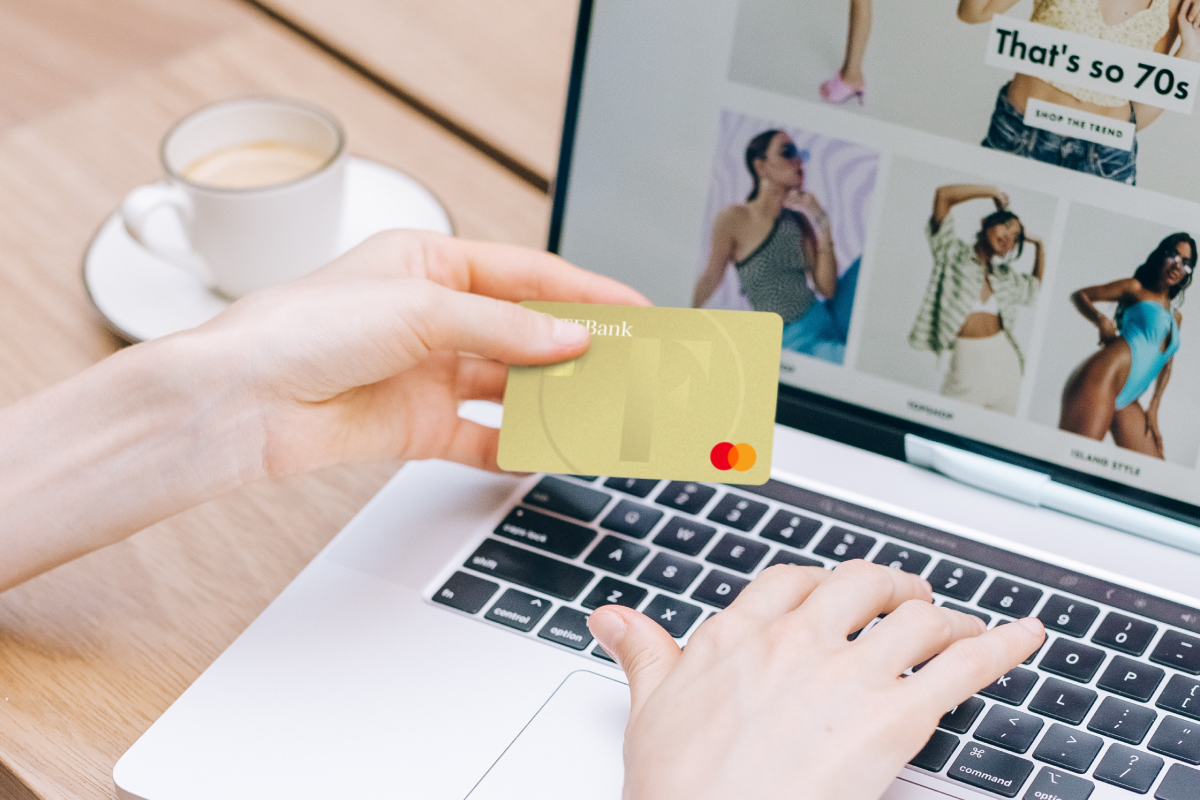 Frau hält Kreditkarte in der Hand, während man auf dem Laptop im Hintegrund einen Online-Shop erkennt