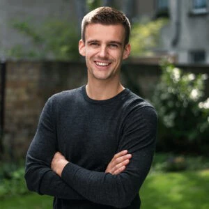 Mann steht mit verschränkten Armen und lächelt in die Kamera