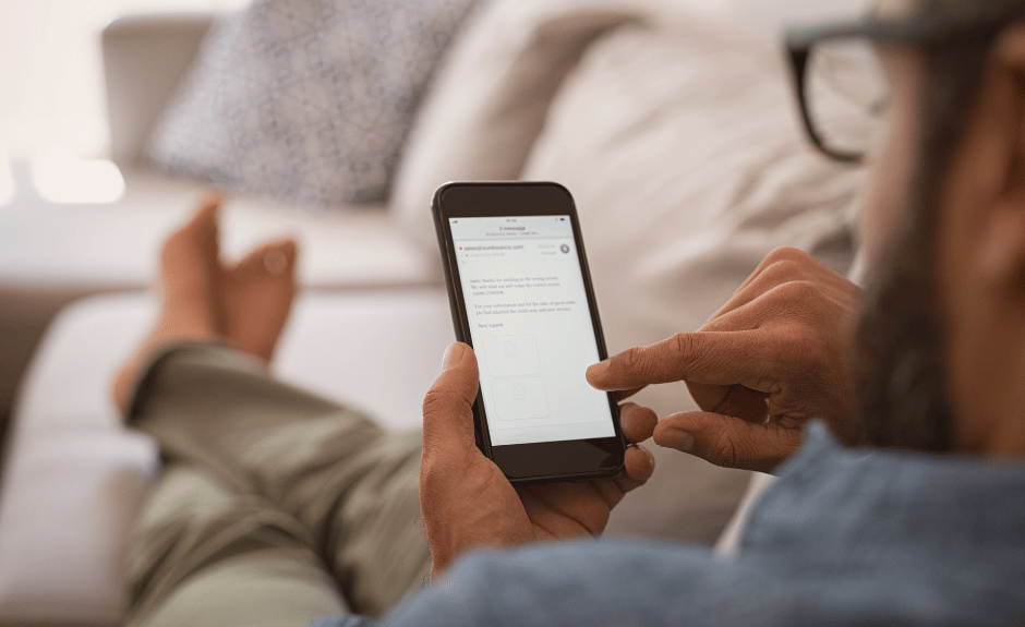 Mann liegt auf der Couch, schaut aufs Handy und liest.