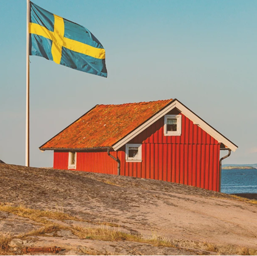 Rotes, schwedisches Haus am Wasser. Neben dem Haus ist eine schwedische Flagge